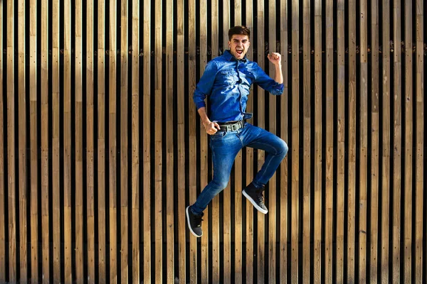 serin ve modern bir hava. ahşap arka plan üzerinde son derece mutlu neşeli tavrı ile atlama yakışıklı seksi erkek kot pantolon kıyafeti,