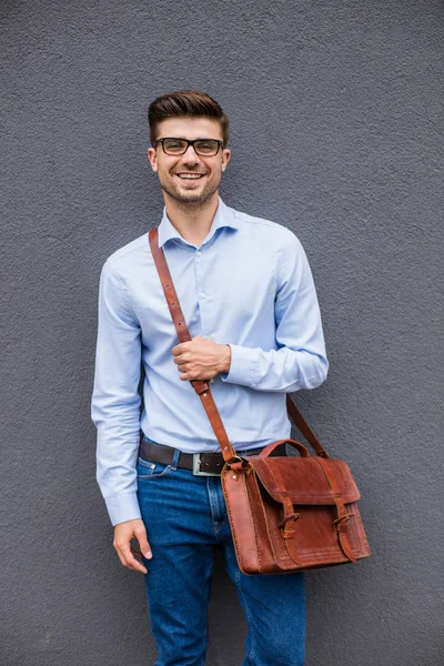akıllı ve güzel. Akıllı casual adam gözlük ve gri arka plan, duvar, kendinden emin ve rahat duran deri çanta