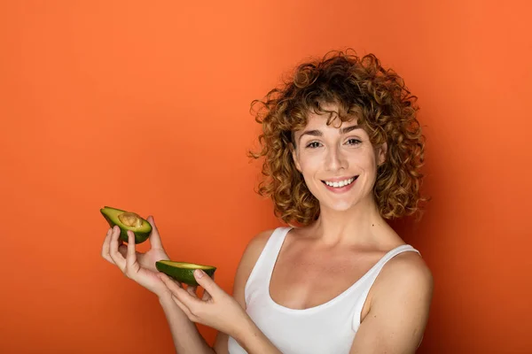 Unga Lockigt Kvinna Som Håller Avokado Händerna Orange Bakgrund — Stockfoto