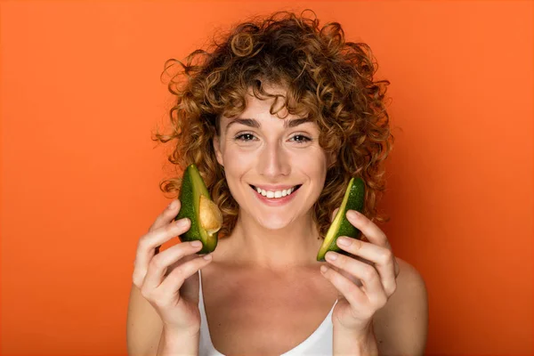 Krullend Jongedame Houden Van Een Avocado Handen Een Oranje Achtergrond — Stockfoto