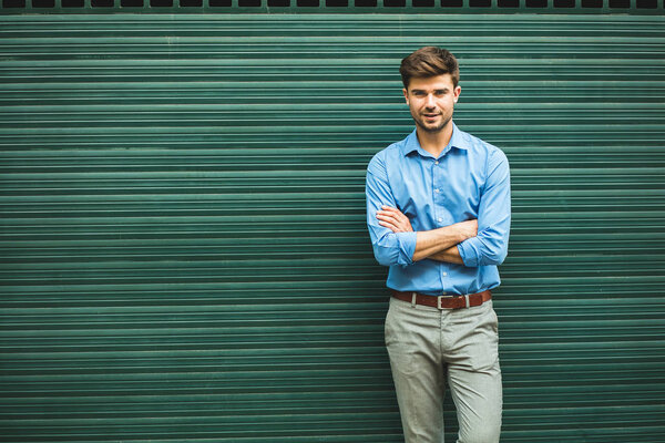 confidence and elegance. handsome elegant man with folded arms resting against a green background and smiling with confidence, and proud