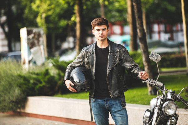 young and cool. handsome man next to his motorcycle, in the center of a city, waiting to ride his bike