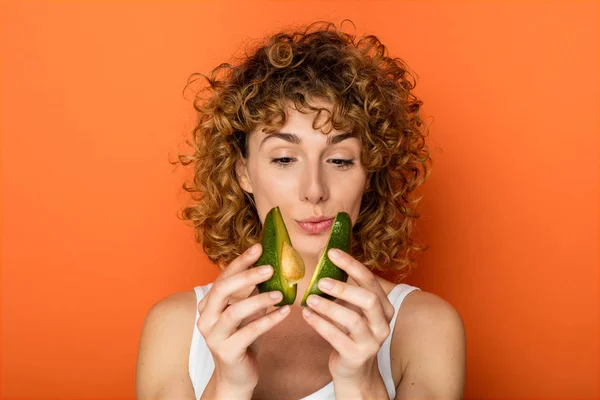 Unga Lockigt Kvinna Som Håller Avokado Händerna Orange Bakgrund — Stockfoto