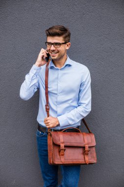 telefon konuşma. yakışıklı akıllı casual adam gözlük ve cep telefonu gri soyut duvar muhabbet deri çanta