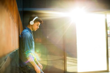 Gençler için müzik. kavram genç adamla tüm kot elbise, güneşten parlama ile odasında kulaklıklar müzik dinleme