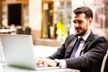 Yakışıklı başarılı adam portresi kahve içmek ve dizüstü bilgisayar, Not defteri, kahve dükkanı, bazı eski şehrin güzel terasta oturup kahvaltı iş adamı oturan ekran bak