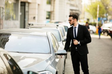 güneş gözlüğü ile takım elbise, onun lüks araba, sokakta bir şehrin içine steping emin zarif adam