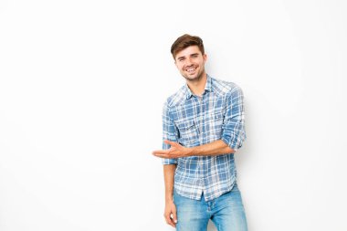 tatlı çocuk, kot pantolon ve kareli gömlek boş uzayda ile beyaz duvarda duran, bir tarafı işaret eden genç adam
