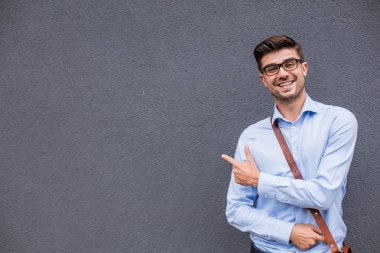Boş tarafı işaret. yakışıklı zeki casual adam gözlük ve güven ve gülümseme ile boş bir alan onun yanında işaret dışında deri çanta