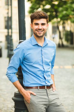 İyi günler ofisinde. Şık gömlek gülümseyen ve metal bir ayağı karşı sokakta oturan genç yakışıklı adam