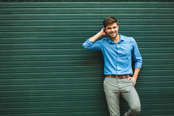confidence and elegance. amused handsome man, elegand dressed, smiling to camera and being relax on a greed background