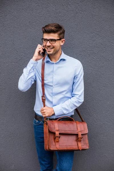 telefon konuşma. yakışıklı akıllı casual adam gözlük ve cep telefonu gri soyut duvar muhabbet deri çanta