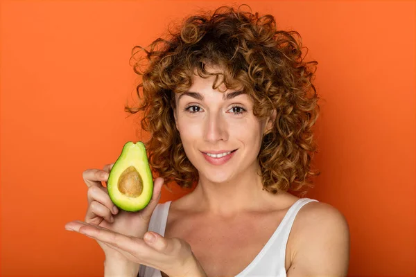 Young Curly Woman Holding Avocado Hands Orange Background — Stock Photo, Image