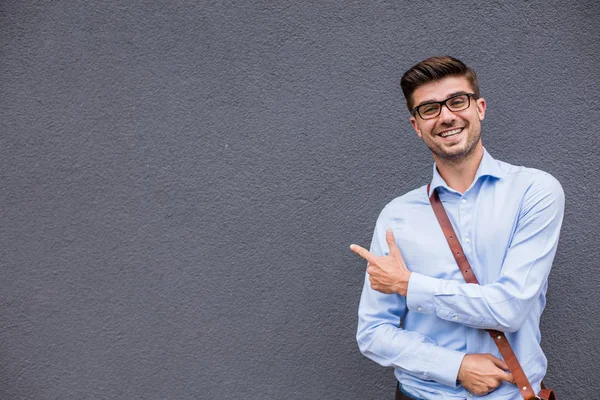 Boş tarafı işaret. yakışıklı zeki casual adam gözlük ve güven ve gülümseme ile boş bir alan onun yanında işaret dışında deri çanta