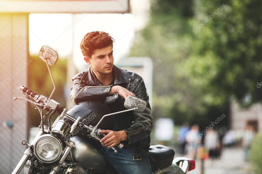 young and cool. handsome man sitting on his motorcycle waiting for someone and relaxing somewhere in a city center