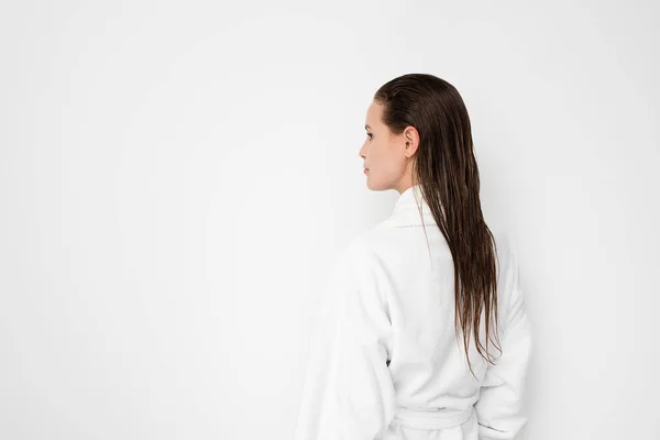 若い女性の後ろの白い背景の上にバスローブ カメラにぬれた髪の毛を示す — ストック写真
