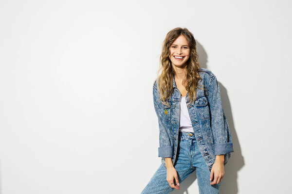 young smiling woman posing to camera in jeans outfit on white background