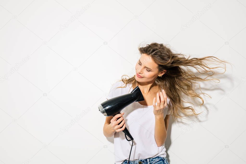 young attractive woman blowing her hair with hair dryer on white background
