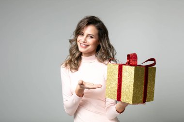 pembe kazaklı gri arka plan üzerinde kamera için altın hediye sunma güzel kadın