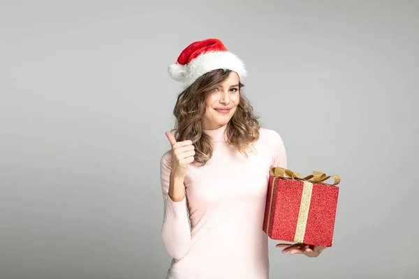 赤い贈り物を手で押しながらカメラに を示すクリスマス帽子を自信を持って女性 — ストック写真
