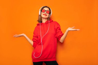 Genç ve güneş gözlüğü ve kulaklık ile kırmızı kapüşonlu asi kız dinleme müzik, serin hipster