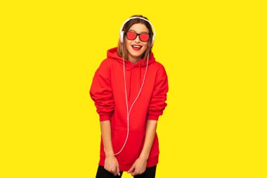 Genç ve güneş gözlüğü ve kulaklık ile kırmızı kapüşonlu asi kız dinleme müzik, serin hipster