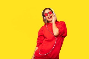 Genç ve güneş gözlüğü ve kulaklık ile kırmızı kapüşonlu asi kız dinleme müzik, serin hipster
