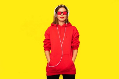 Genç ve güneş gözlüğü ve kulaklık ile kırmızı kapüşonlu asi kız dinleme müzik, serin hipster