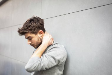 ağrı boyun, eller gri duvar ve boynunda olan genç adam