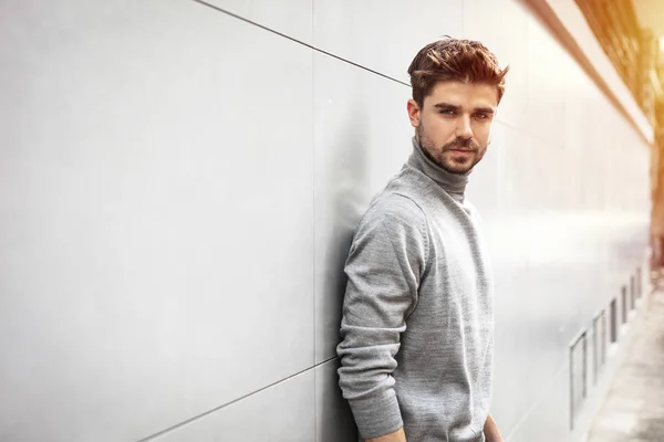 portrait of a cool man posing outside next to a gray modern wall