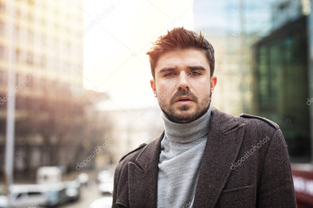 handsome man looking with confidence to camera, outside with office buildings in background