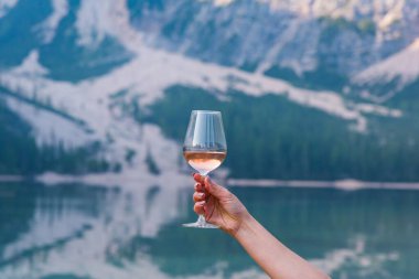 Genç bayan, sabahın köründe Braies Gölü 'nde elinde bir bardak şarapla arka planda yeşil ormanla.