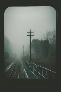 Demiryolunda karanlık, soğuk bir sabah. Önünde derin bir sis ve sağ tarafında da sütunlar var.