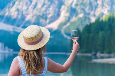 Soğuk bir sabahta Lago di Braies sahilinde elinde bir bardak şarap tutan şapkalı gezgin kız.
