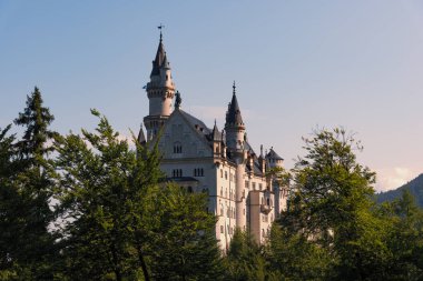 Güneş ışınlarında görkemli Neuschwanstein şatosu. Barışçıl hava koşullarında arka planda açık bir gökyüzü var.