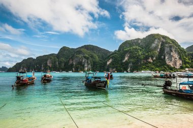 Phi Phi, Tayland - 4 Temmuz 2015: Tayland 'da Pi Pi Adaları sınırındaki geleneksel ahşap teknenin arka planında yeşil dağlar