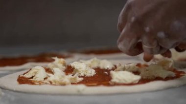 Yakın çekim hangi domatese Yapıştır sürülür, bir pizza daire ve eşit mozzarella peynir parçaları koyar bir Şef, elleri. Arka planda pizza için diğer daireler vardır.