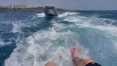 Bir adam bacakları suda yüzen bir gemide otururken sallıyor. Sprey gidin. Teknenin motor kaynar su yolu. Tekne bir tekne bir ip bağladılar taşır. Açık denizde kıyıdan yelken açtı,.