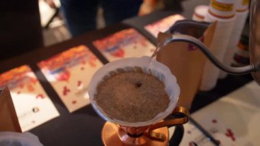 Diğer insanların önünde adam Purover altın renkli masada kahve yapıyor. Dairesel bir hareketle metal bir su ısıtıcısı üzerinden dökülen su.