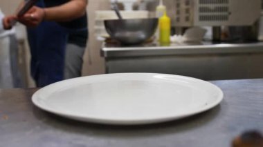Bir adam bir mavi önlük giyen bir mutfakta pizza bir spatula ile uzun kırmızı bir işleci kullanılarak bir beyaz yuvarlak tabağına koyuyor. Pizza hala tereyağı kaynıyor. Buhar geliyor.