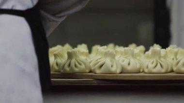 Pişmiş mantas ahşap bir stand üzerine yalan close-up. Onları kim mantas birini hazırlar ve bu zaten yerleştirmektedir bir mavi önlük bir kadın yatıyor