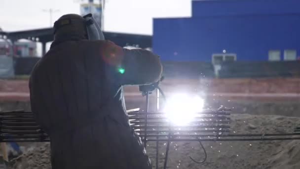 一个穿着特殊灰色衣服的人用一种特殊的工具焊接金属格子 焊接的地方是黄色的火花 面部焊接面罩 从后面的街道上开枪 晚上的时间 — 图库视频影像