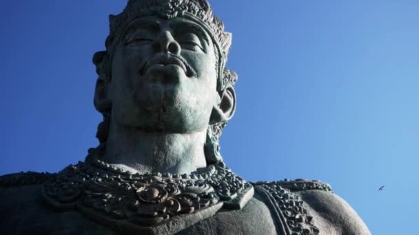 バリ島 インドネシア 2018 下から青い空に対して神ビシュヌ神の石像の頭を 鳥が空を飛ぶし 像の顔まで飛ぶ — ストック動画