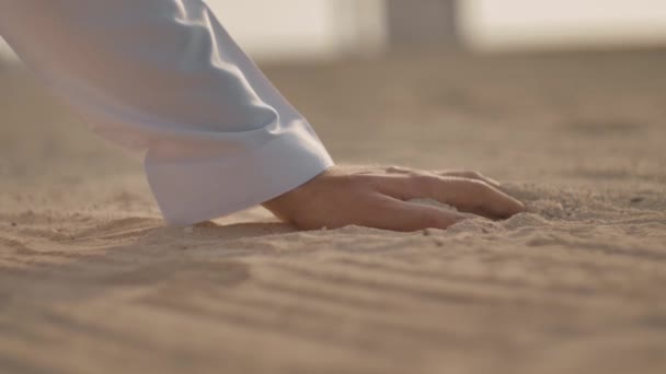 一个穿着白色衣服的白人男子的手的特写镜头 他把手放在沙子上 把它拿成拳头 然后倒回去 手里把它翻过来 侧视图 — 图库视频影像