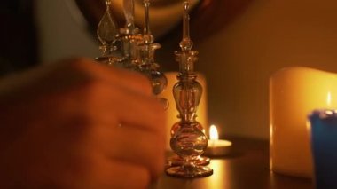 Masanın üzerinde odada büyük/küçük mumlar ve kavisli cam şişeler vardır. Bir adam elini tutar ve bir şişe alır. Duvarda bir ayna var. Muhteşem, mistik bir tema. Yan görünüm.
