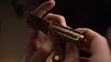 Bir adam numaraları ile bakır kriptex tutar. Kriptex kodunu eli ile hesaplıyor. Cryptex sonunda, bir deri kayış Mans parmak konur. Odada loş bir ışık vardır. Closeup.