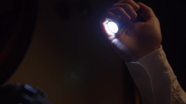 Dans le poing d'un homme est une petite lampe de poche LED. La pièce est sombre, l'homme allume la lampe de poche et inspecte l'objet devant lui. Une main en blanc et une lampe de poche - gros plan. Fabuleux, système mystique 