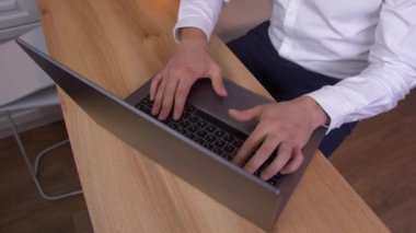 Beyaz gömlek ve mavi pantolon bir adam parlak bir oda/kafede açık ahşap masada otururken gri metalik dizüstü bilgisayarda çalışıyor. Yukarıdan görüntüle. panoramik çekim. Eller yakın çekim.