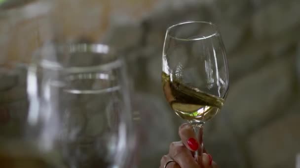 赤い釘を持つ女性の手に白ワインのグラス ワインを味わう女性が グラスで軽く振る テイスティングのコンセプト 他の空のグラスを背景にワインのグラス — ストック動画