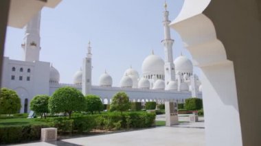 Bae, Abu Dabi - Eylül 2018. Yüksek spiers ve kubbeler ile Şeyh Zayed Beyaz Camii iç avlunun güzel bir görünüm. Düzgünce kesilmiş yeşil çalılar ve ağaçlar.